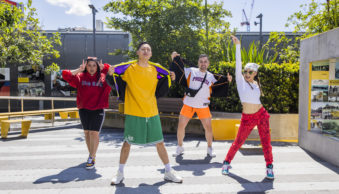 Four dancers in various poses wearing colourful sports gear. They are outdoors,